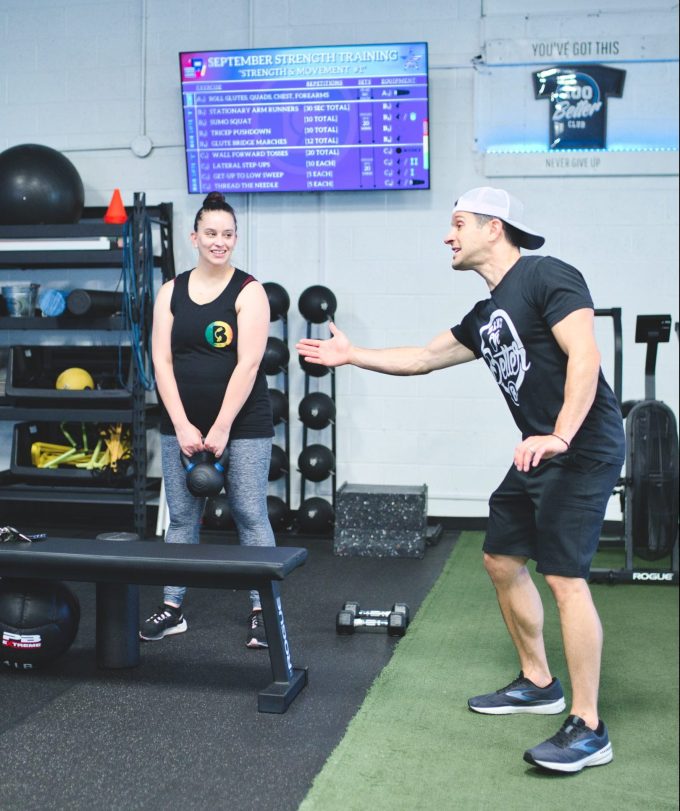 a personal trainer assisting a gym member how to correctly lift a kettlebell