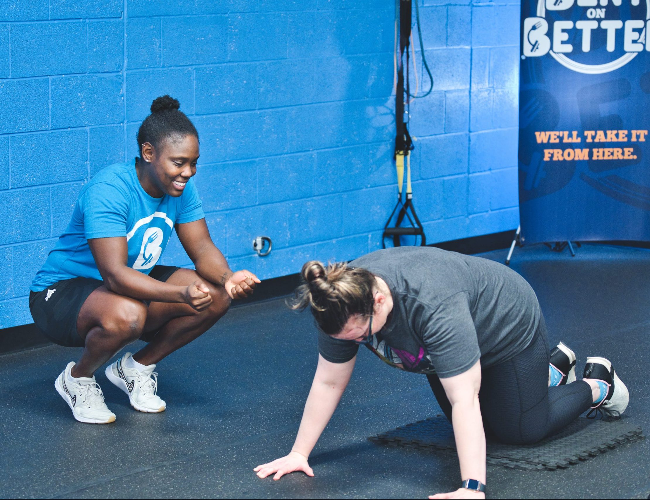 a woman doing a push-up and assisted by a trainer in a gym