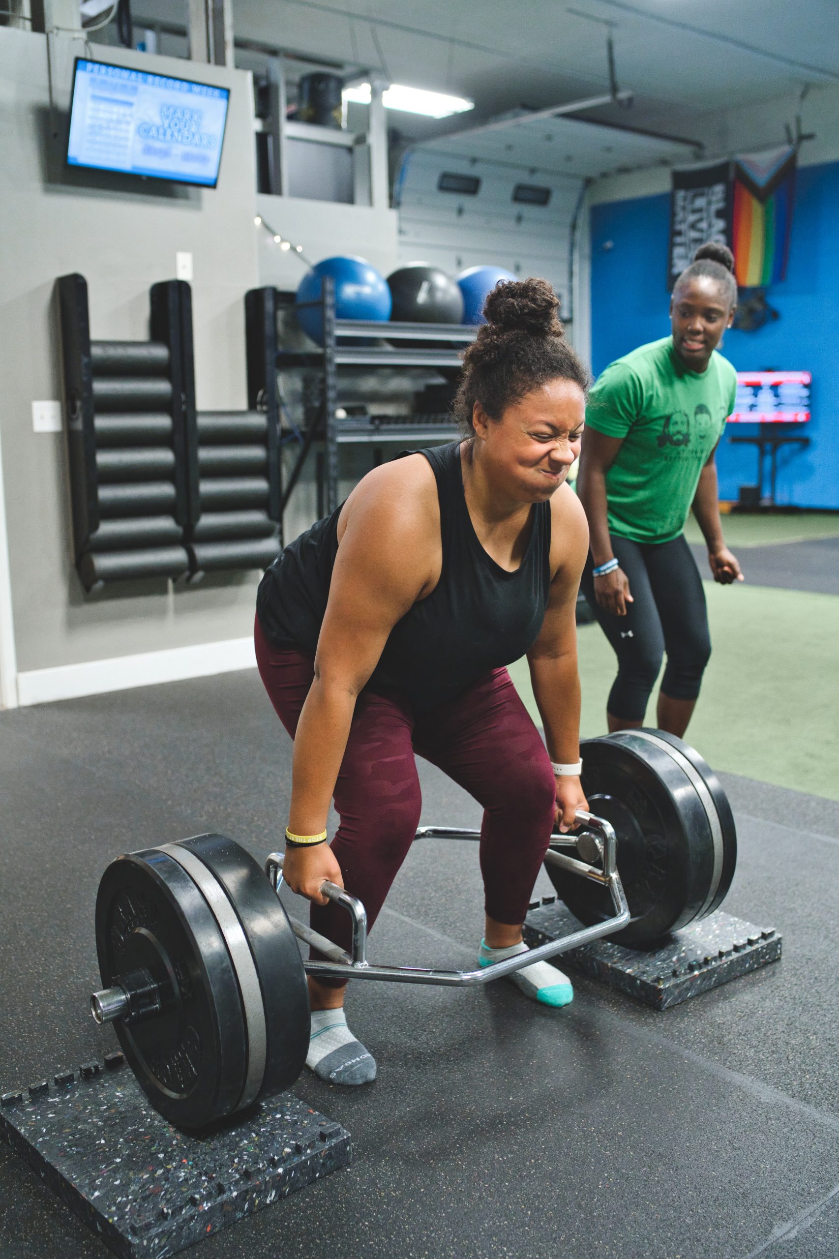 a woman deadlifting a trap bar with a coach beside her